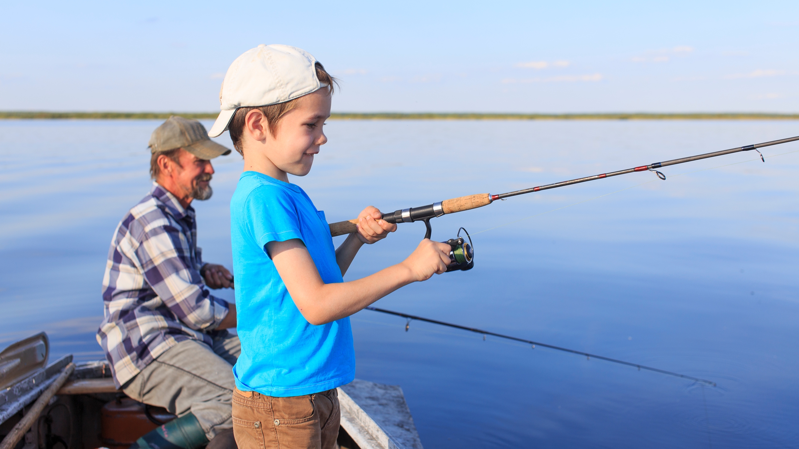 A young angler fishing from a boat with an adult nearby